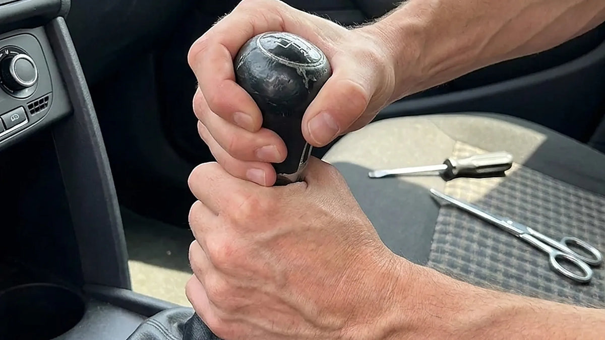 Conducteur qui tire à deux mains sur un pommeau de vitesse usé qui refuse de sortir du levier Image