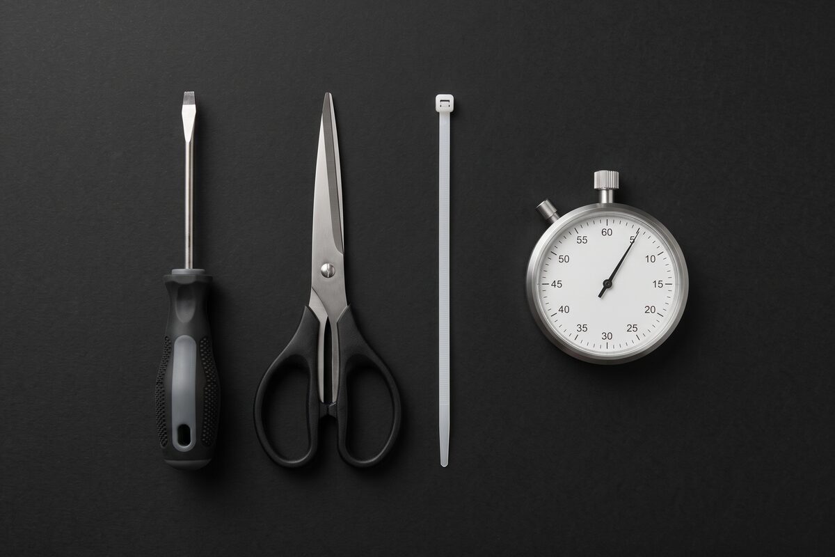 Tournevis plat noir, ciseaux noir, colson blanc et chronomètre sur fond noir Image
