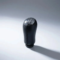 Pommeau de vitesse Clio 3 couture noire, vue produit isolée avec surpiqûres noires apparentes et schéma des vitesses gravé