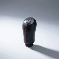 Pommeau de vitesse Clio 3 couture rouge, vue produit isolée avec surpiqûres rouges apparentes et schéma des vitesses gravé